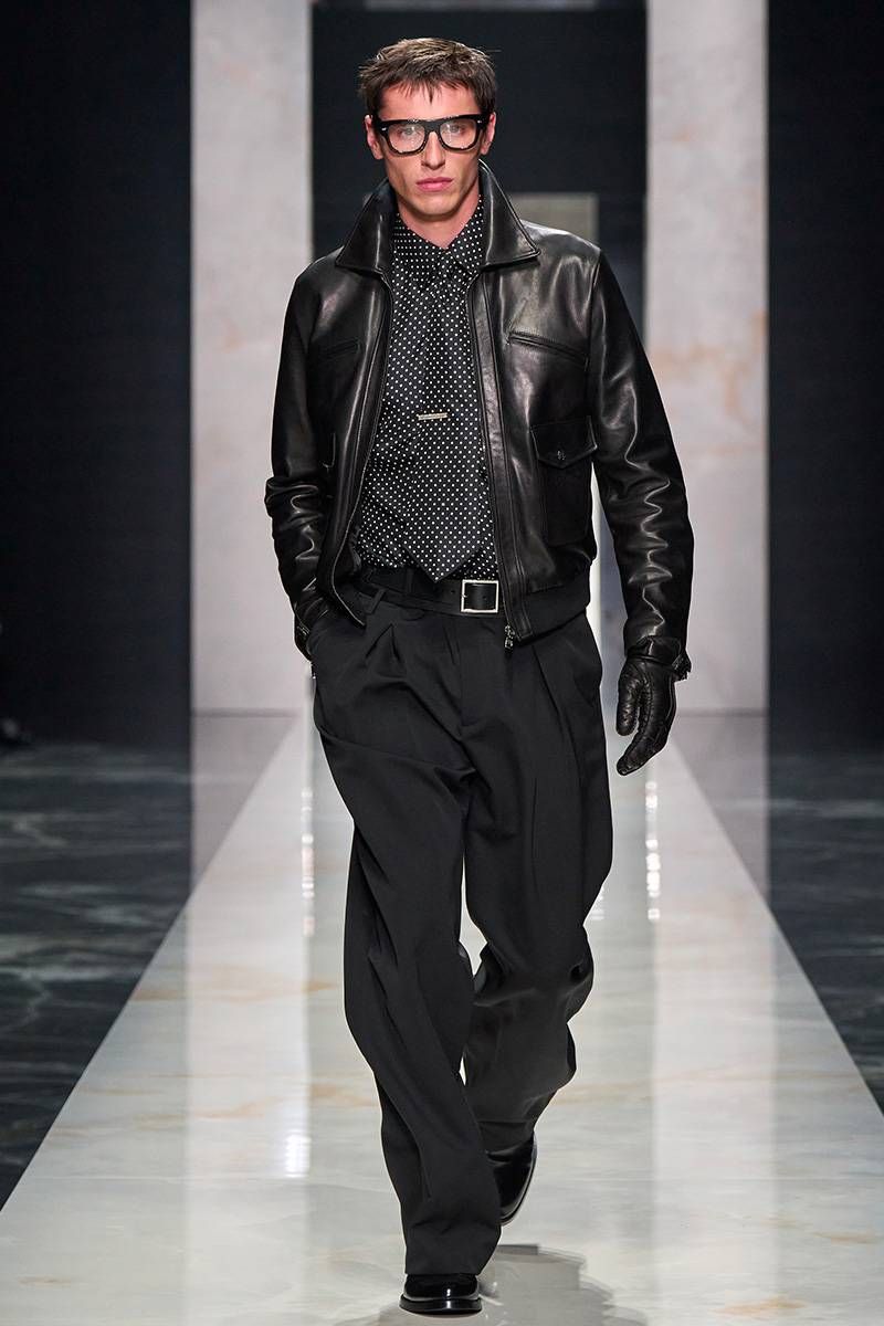 Dolce & Gabbana menswear look with a leather jacket, polka-dot shirt, tailored trousers, gloves and glasses, balancing sharp tailoring and restraint in a season focused on intention over spectacle.